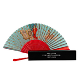 A fortune teller folding fan with a red design when closed, opened to show detailed illustrations. It is displayed next to its black gift box with the museum's name embossed in silver.